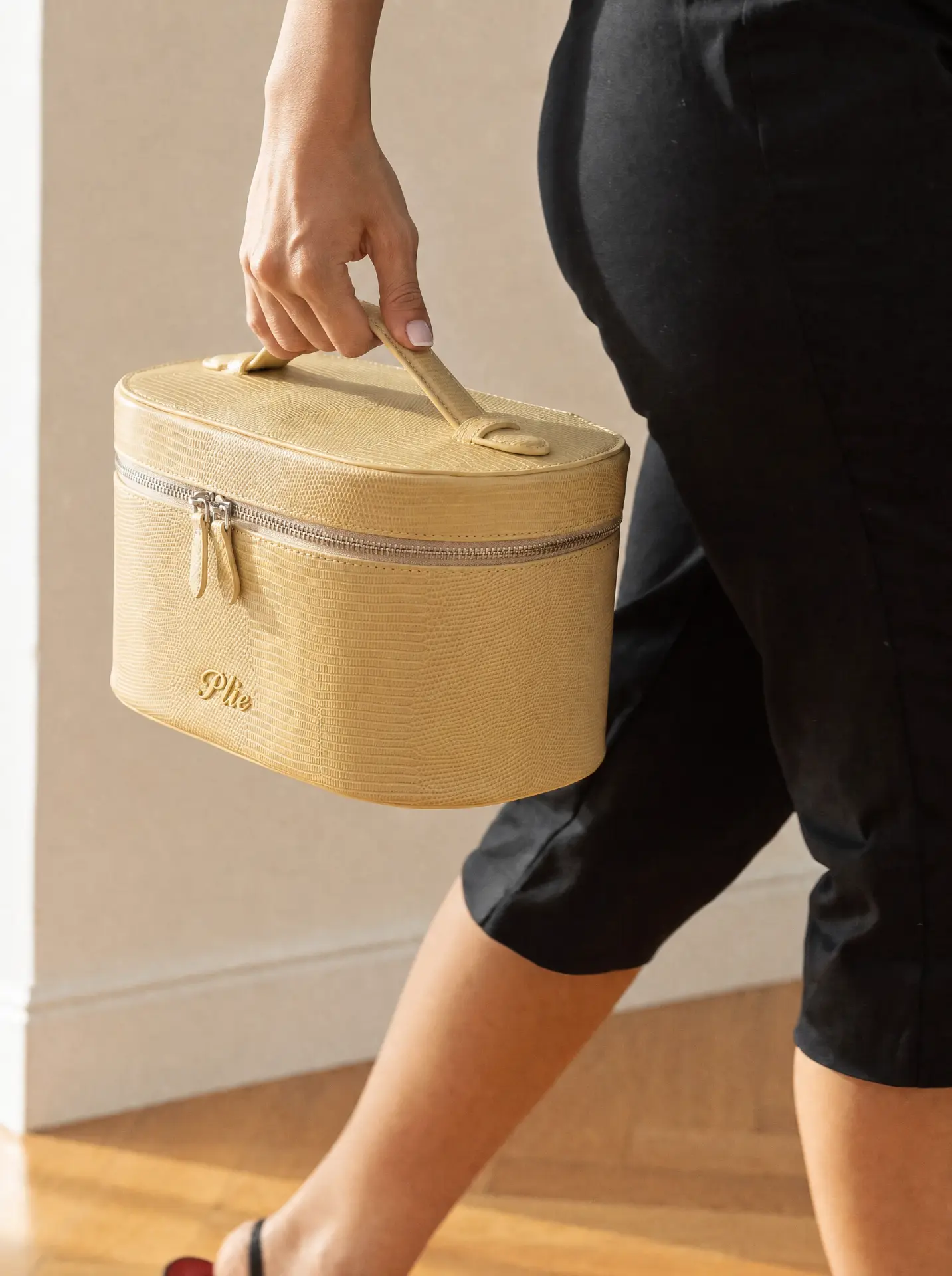 OSTIR Travel Case in butter lizard-embossed finish with ONYX & OAK logo, carried in hand